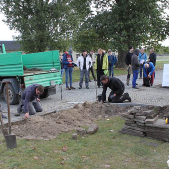 Auszubildende setzen im Bereich der Häftlingswäscherei neue Bordsteine.